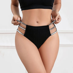 A woman holding up black ribbed high-waisted briefs with three sparkling elastic straps on the sides.