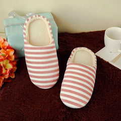 A pair of red and white striped plush indoor slippers on a brown rug next to a gift box.