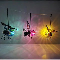 Three metal bee-shaped solar lights hanging and casting colorful light on a wall.