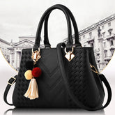 A black leather-look handbag with a chevron pattern and a pompom tassel keychain.