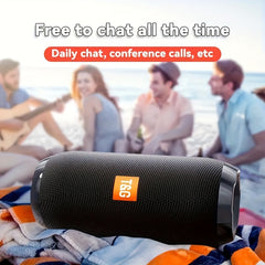 A black cylindrical Bluetooth speaker on a beach towel with a blurred group of friends in the background.