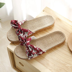 A pair of burgundy floral slides with a fabric bow on a wooden surface.