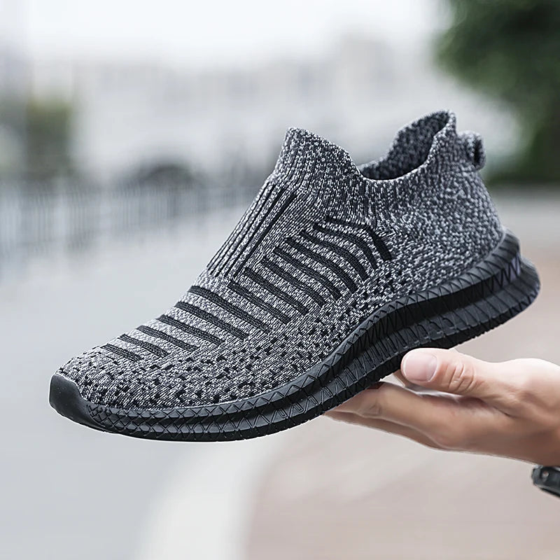 Hand holding a gray and black knit slip-on sneaker.