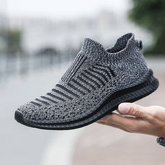 Hand holding a gray and black knit slip-on sneaker.