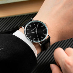 Minimalist black dial watch with 24-hour marks and leather band.